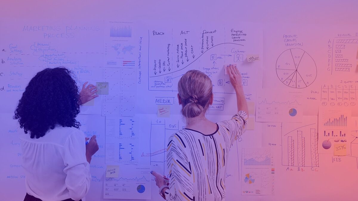 Two marketing experts analyze strategies and data on a whiteboard covered with diagrams and charts on the topic of sustainability communication.